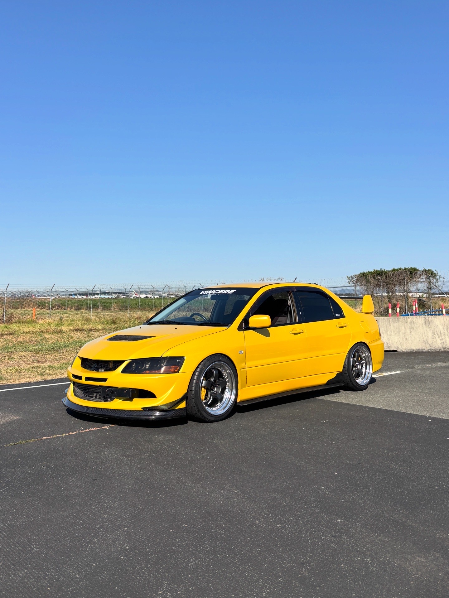 Yellow Mitsubishi Evo VIII on a sunlit circuit apron