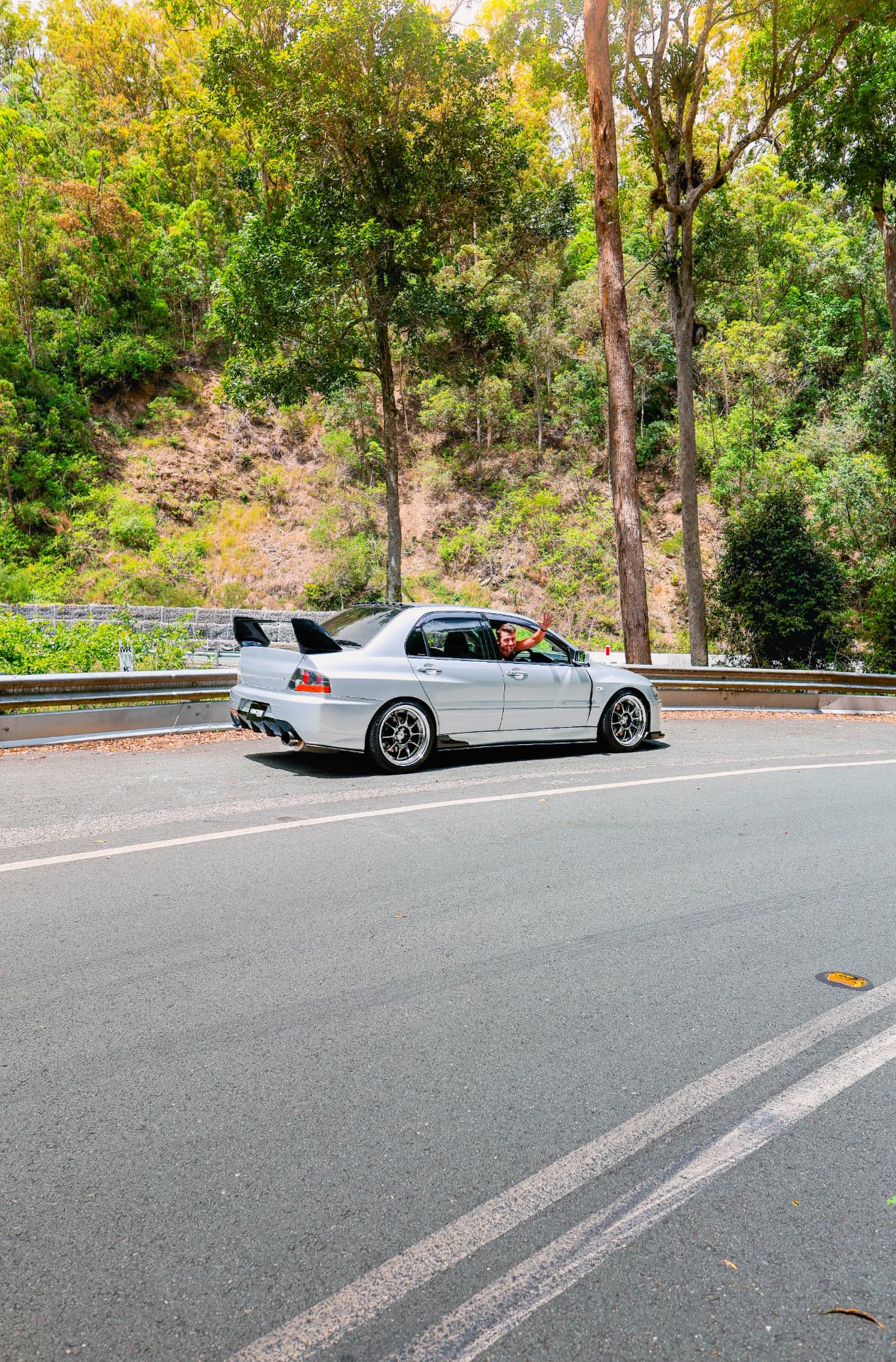 Driver waving from a silver Evo on a forest road