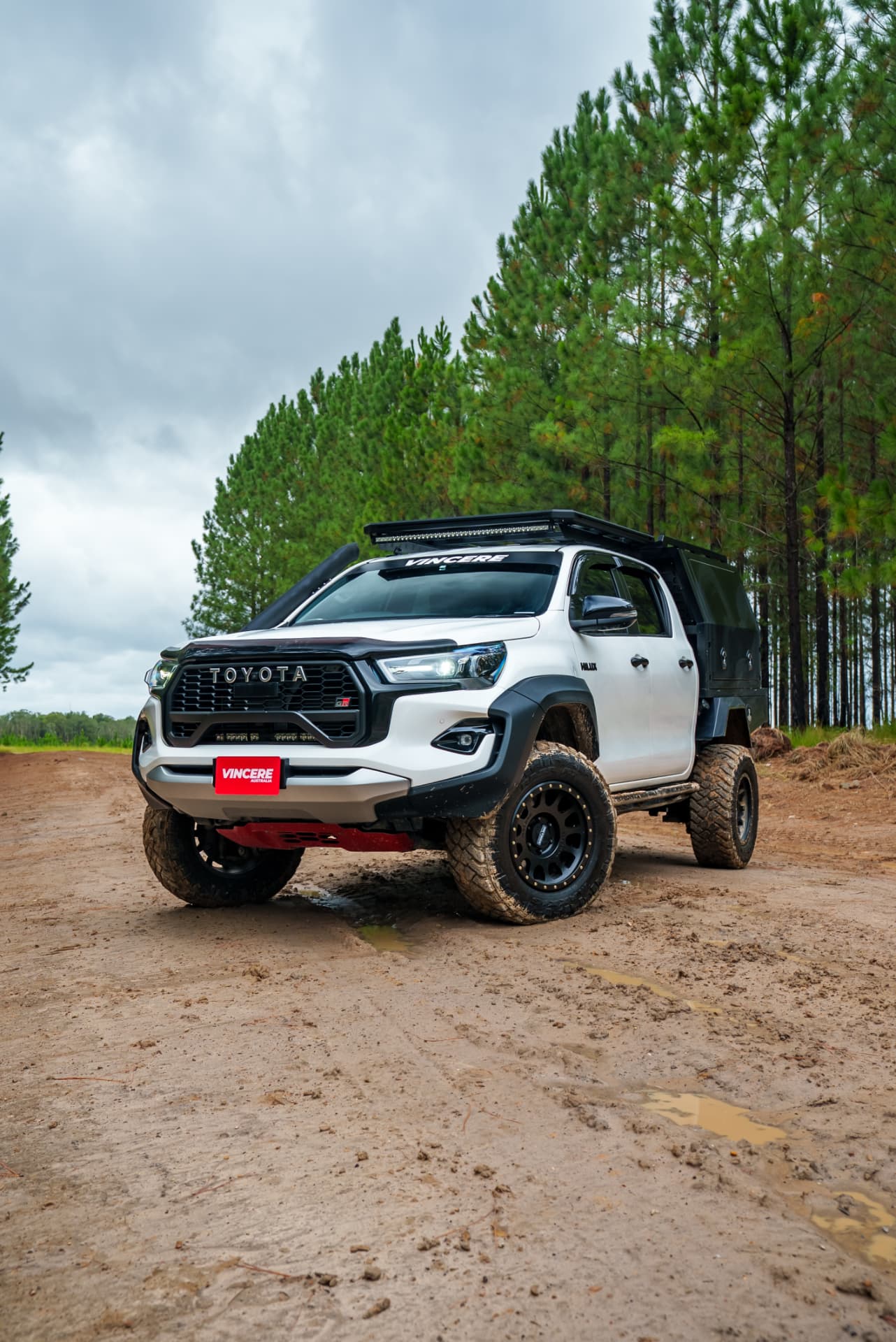 HiLux touring rig on a dirt road beside pine forest