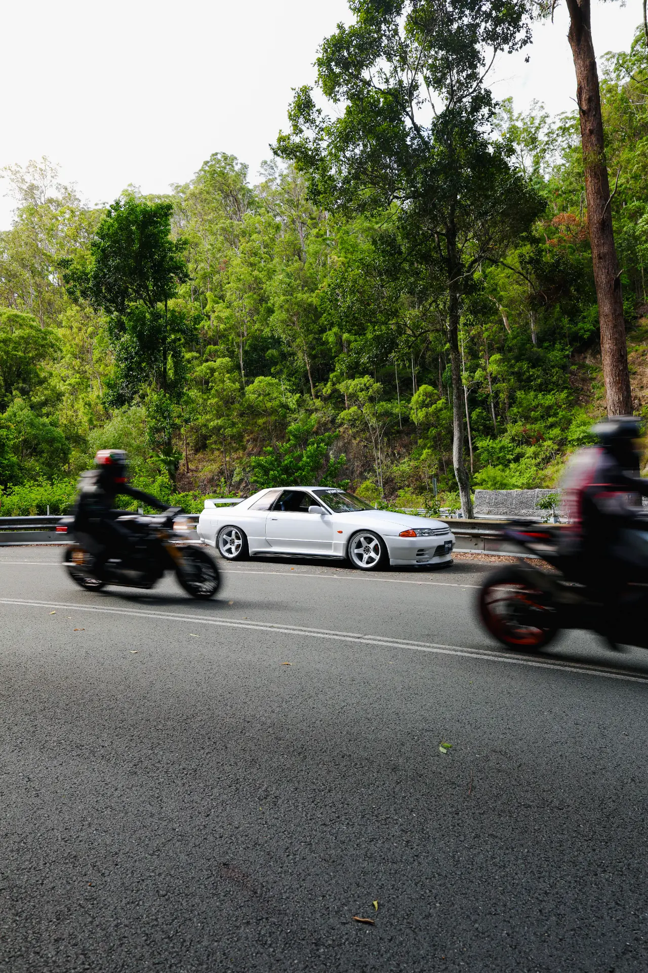 White R32 GT-R parked on a mountain road as motorcycles pass