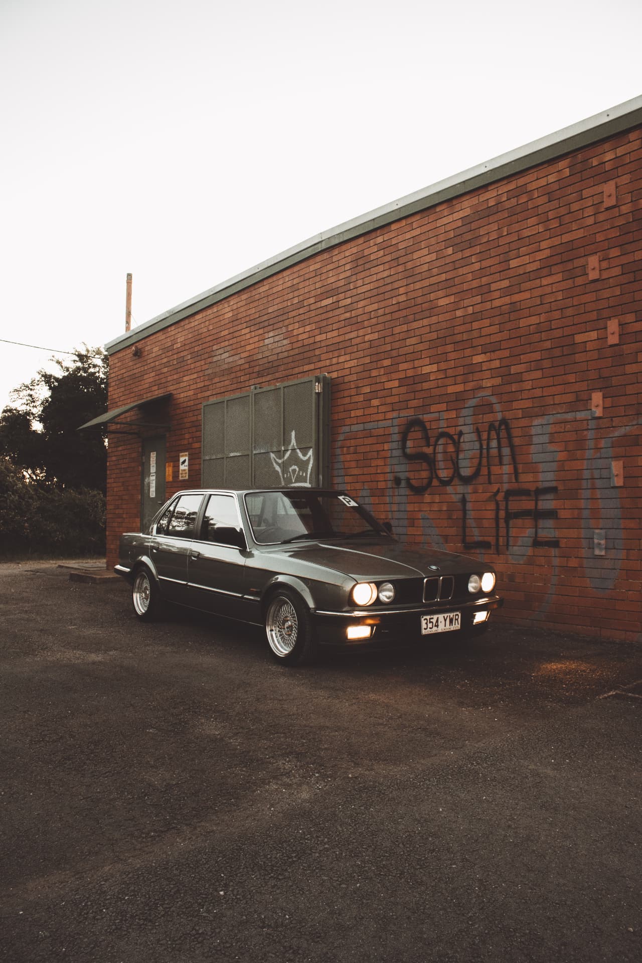 BMW E30 on BBS wheels beside a graffitied brick warehouse