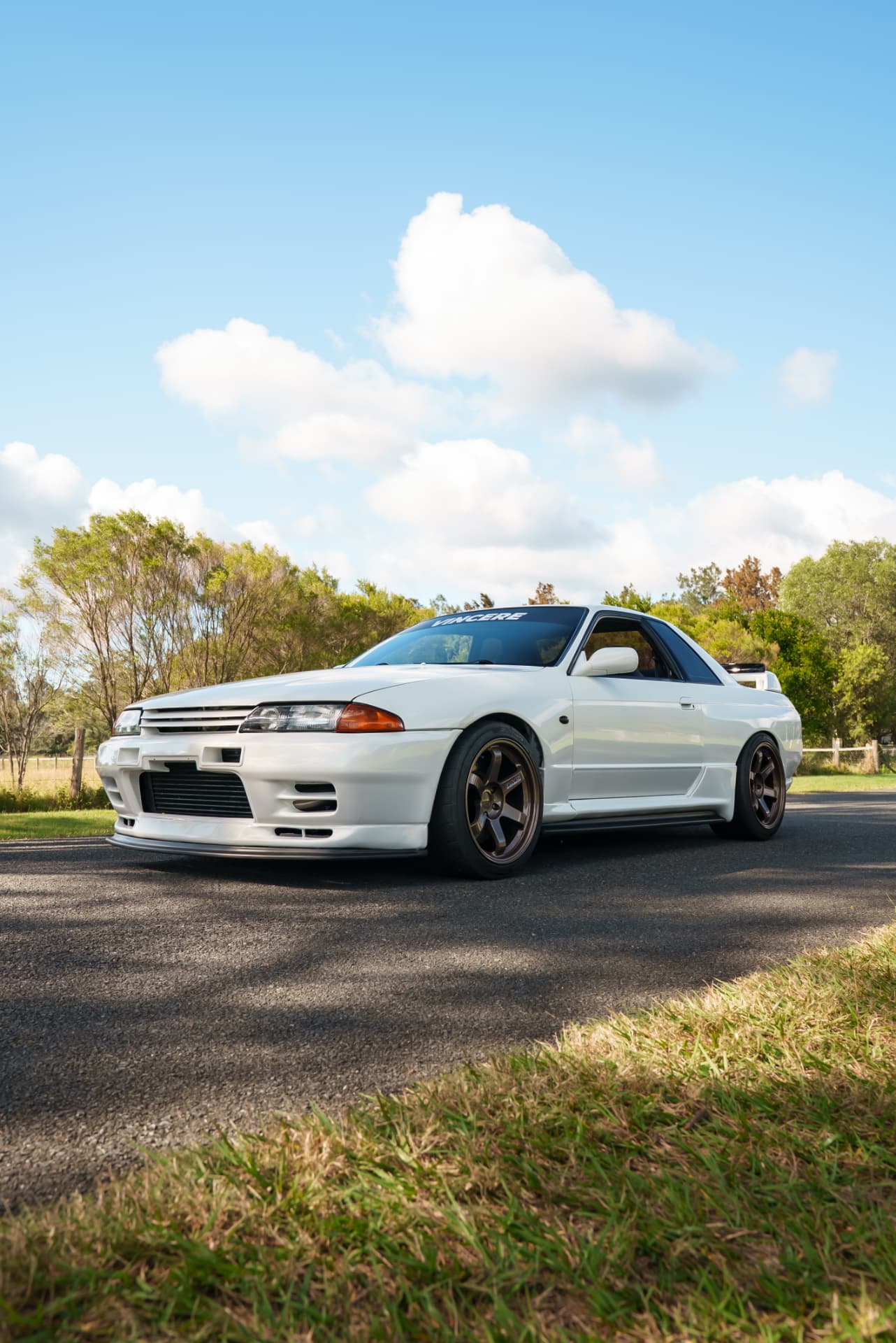 Front three-quarter of a white Nissan Skyline R32 on a country road