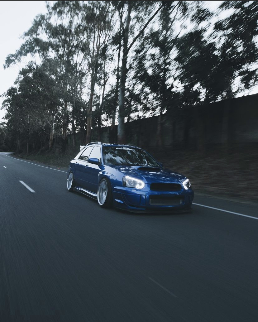 Blue Subaru WRX wagon rolling shot on a tree-lined road