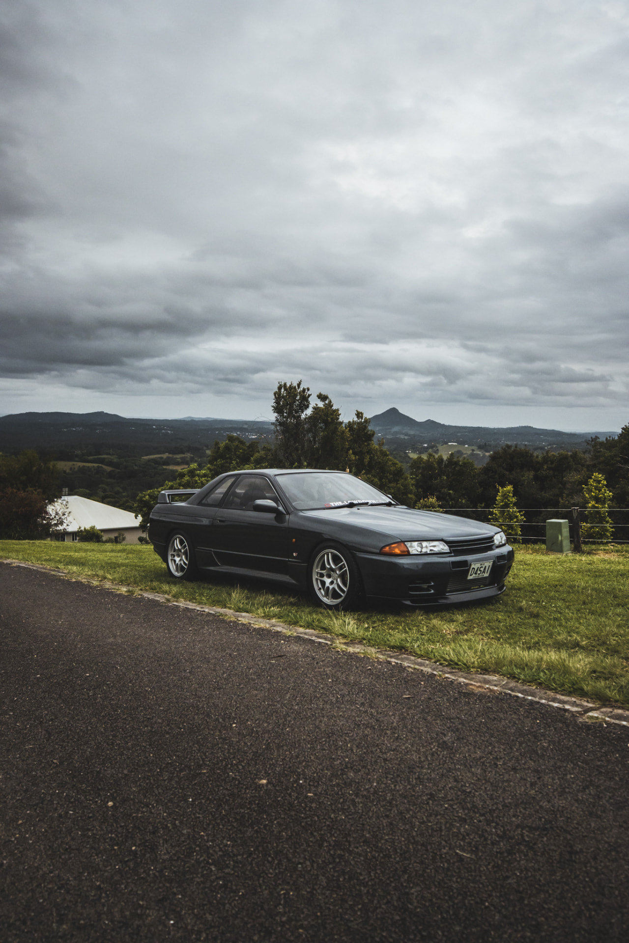 Grey Nissan Skyline R32 GT-R on a grassy ridge under storm clouds