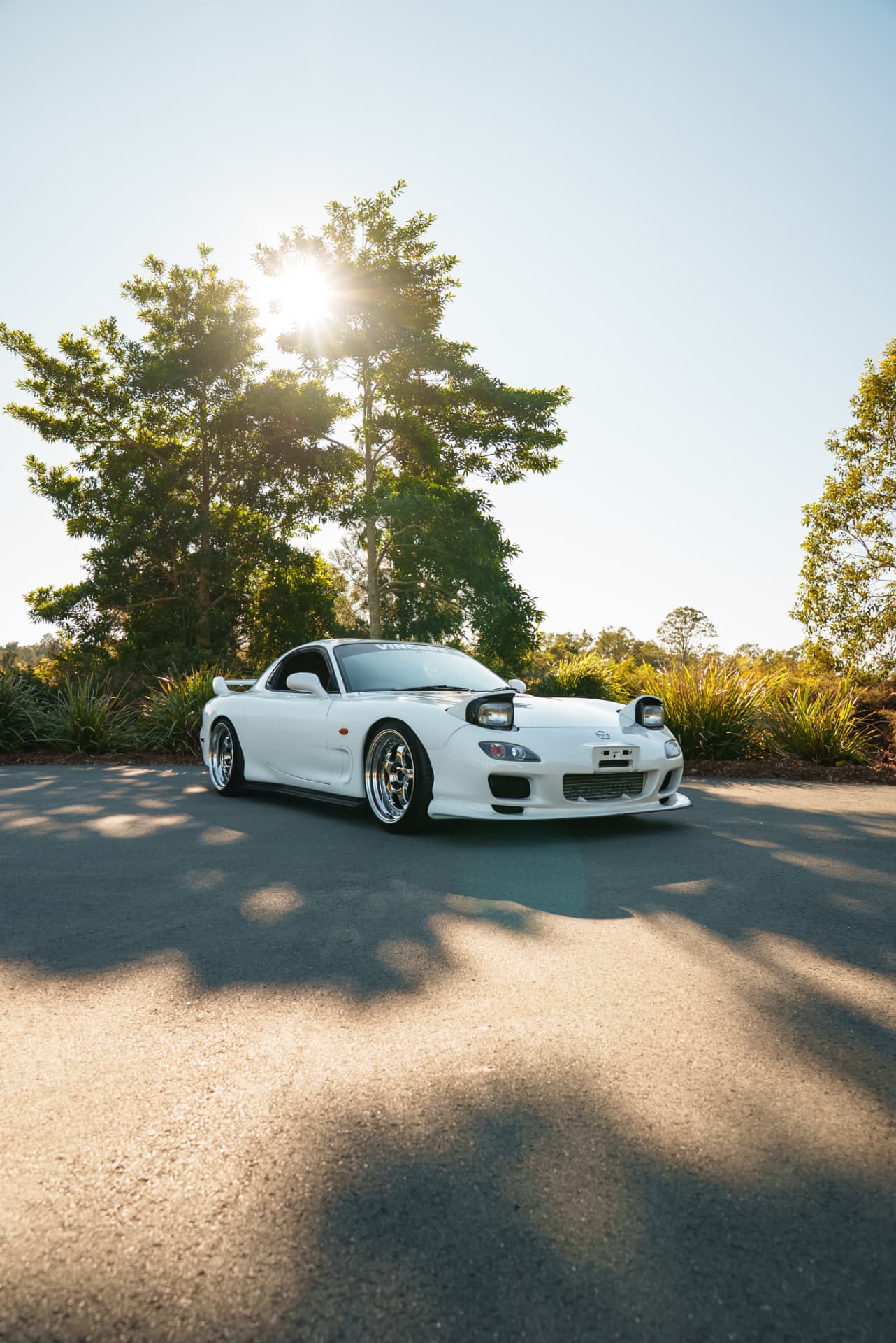 White Mazda RX-7 FD on a country road with sun flare through the trees