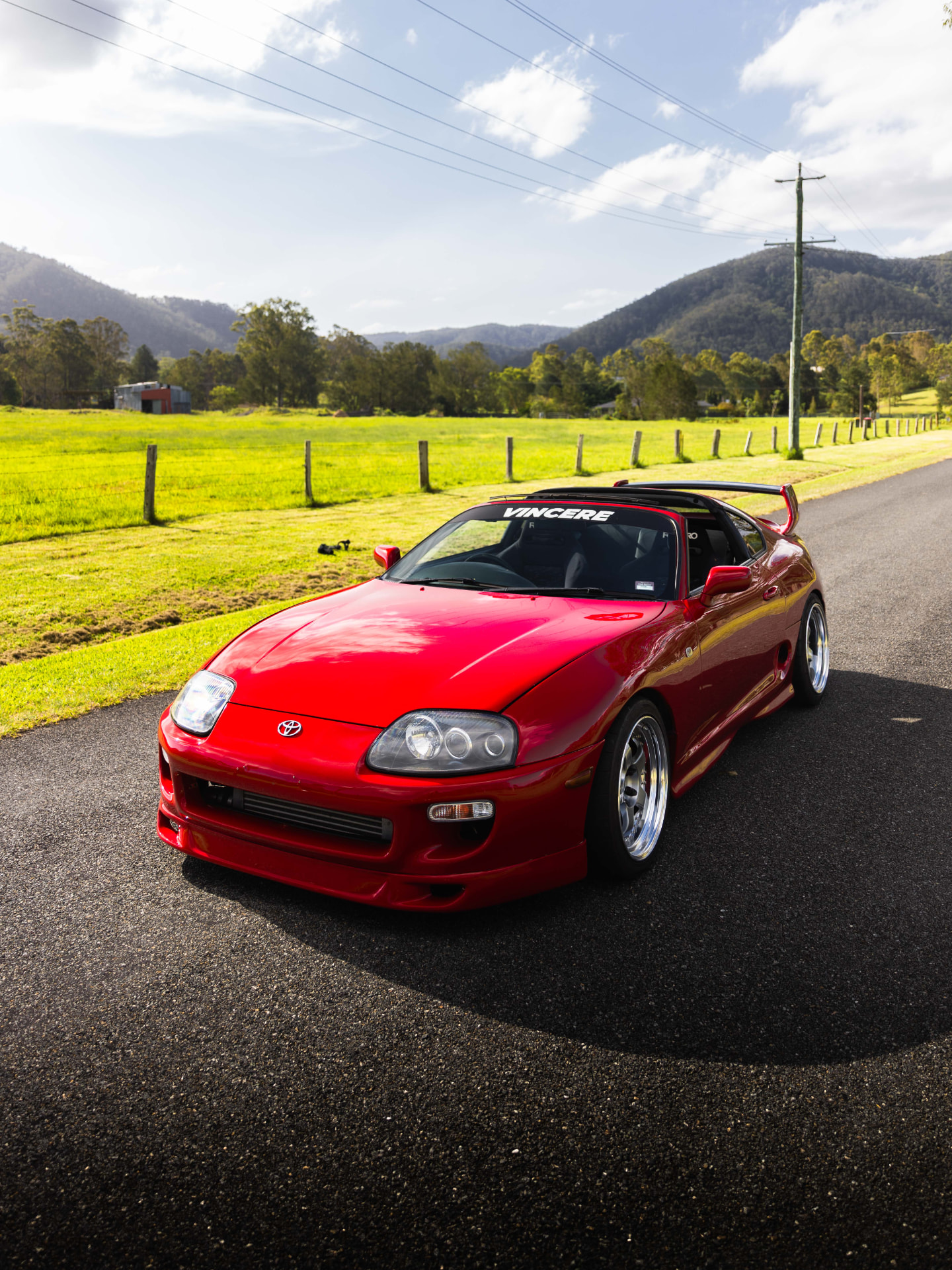 Red Toyota Supra MK4 front three-quarter with hinterland hills behind